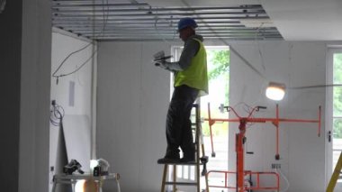 Hard male work on construction site. Two professional workers in special uniforms Contractors Safety Hats repairing ceiling wall inside building. Builders equipment at workplace. industrial premises.