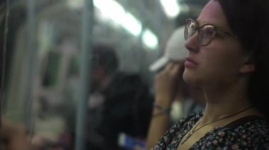 Close shot of young attractive Ukraine female in glasses sitting on moving city metro train. Woman calling typing text message on mobile phone. Pretty Lady waving hands say goodbye. Traveling alone.
