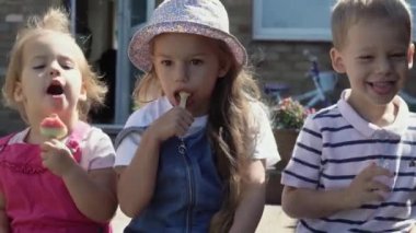 Three cute little Children enjoys delicious ice cream cone. Child eating watermelon popsicle. Kids Siblings snack sweets in Home Garden. Summer holiday Hot weather Sunny Day. Childhood, Food Candy.