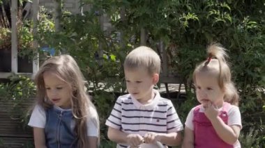 Portrait of Cute Little Three Children sitting on the beanch Garden. Cheerful Carefree Childhood. Preschool Siblings Friends Feeling Free Funky, Good Emotions Life. Home Dancing. Friendship Kids.