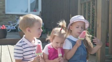 Three cute little Children enjoys delicious ice cream cone. Child eating watermelon popsicle. Kids Siblings snack sweets in Home Garden. Summer holiday Hot weather Sunny Day. Childhood, Food Candy.