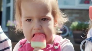 Close up portrait little Toddler girl enjoys delicious ice cream cone. Dirty Child Face eating popsicle. Kid snack sweets in Home Garden. Summer holiday Hot weather Sunny Day. Childhood, Food Candy.