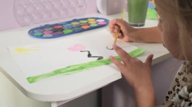Talented Creative Child Girl Female Artist Draws with Her Hands on Paper, Using Fingers Paints Brush Creates Colorful, Kid Drawing on table at Home. Painter Creating Abstract Modern Art. Childhood.