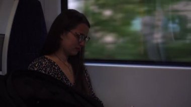 Close shot of young attractive Ukraine female in glasses sitting on moving city metro train. Woman calling typing text message on mobile phone. Pretty Lady waving hands say goodbye. Traveling alone.