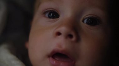 Baby boy sucks nipple at Evening. Smiling portrait of little child. Happy Family. Close-up sleepy Face of Child Eyes While looking at the camera in the dark. Infant, Childhood, Childcare, Motherhood.