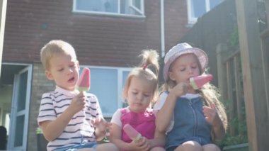 Three cute little Children enjoys delicious ice cream cone. Child eating watermelon popsicle. Kids Siblings snack sweets in Home Garden. Summer holiday Hot weather Sunny Day. Childhood, Food Candy.