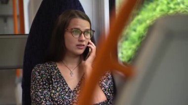 Close shot of young attractive Ukraine female in glasses sitting on moving city metro train. Woman calling typing text message on mobile phone. Pretty Lady waving hands say goodbye. Traveling alone.