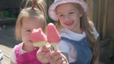 Two Sisters Children enjoys delicious ice cream cone. Child eating watermelon popsicle. Kids Siblings snack sweets in Home Garden. Summer holiday Hot weather Sunny Day. Childhood, Food Candy Friends.
