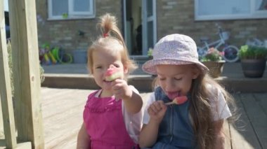Two Sisters Children enjoys delicious ice cream cone. Child eating watermelon popsicle. Kids Siblings snack sweets in Home Garden. Summer holiday Hot weather Sunny Day. Childhood, Food Candy Friends.