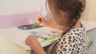 Talented Creative Child Girl Female Artist Draws with Her Hands on Paper, Using Fingers Paints Brush Creates Colorful, Kid Drawing on table at Home. Painter Creating Abstract Modern Art. Childhood.