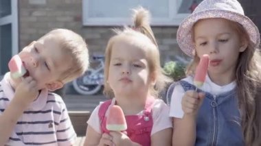 Three cute little Children enjoys delicious ice cream cone. Child eating watermelon popsicle. Kids Siblings snack sweets in Home Garden. Summer holiday Hot weather Sunny Day. Childhood, Food Candy.