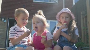 Three cute little Children enjoys delicious ice cream cone. Child eating watermelon popsicle. Kids Siblings snack sweets in Home Garden. Summer holiday Hot weather Sunny Day. Childhood, Food Candy.