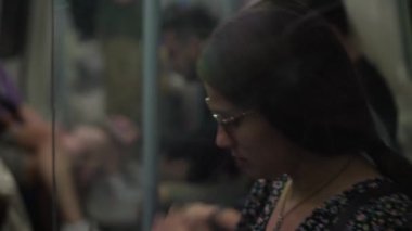 Close shot of young attractive Ukraine female in glasses sitting on moving city metro train. Woman calling typing text message on mobile phone. Pretty Lady waving hands say goodbye. Traveling alone.