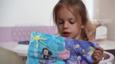 Talented Creative Child Girl Female Artist Draws Ranbow Mother summer on Paper, Child showing her work.Creates Colorful, Kid Drawing on table at Home. Painter Creating Abstract Modern Art. Childhood.