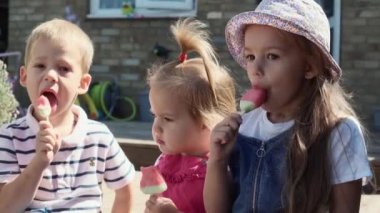 Three cute little Children enjoys delicious ice cream cone. Child eating watermelon popsicle. Kids Siblings snack sweets in Home Garden. Summer holiday Hot weather Sunny Day. Childhood, Food Candy.