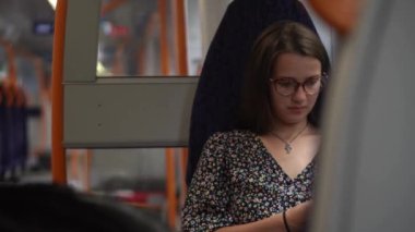 Close shot of young attractive Ukraine female in glasses sitting on moving city metro train. Woman calling typing text message on mobile phone. Pretty Lady waving hands say goodbye. Traveling alone.