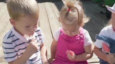 Three cute little Children enjoys delicious ice cream cone. Child eating watermelon popsicle. Kids Siblings snack sweets in Home Garden. Summer holiday Hot weather Sunny Day. Childhood, Food Candy.