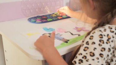 Talented Creative Child Girl Female Artist Draws with Her Hands on Paper, Using Fingers Paints Brush Creates Colorful, Kid Drawing on table at Home. Painter Creating Abstract Modern Art. Childhood.