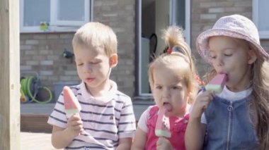 Three happy little Children enjoys delicious ice cream cone. Child eating watermelon popsicle. Kids Siblings snack sweets in Home Garden. Summer holiday Hot weather Sunny Day. Childhood, Food Candy.