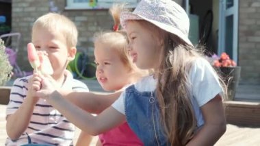 Three cute little Children enjoys delicious ice cream cone. Child eating watermelon popsicle. Kids Siblings snack sweets in Home Garden. Summer holiday Hot weather Sunny Day. Childhood, Food Candy.