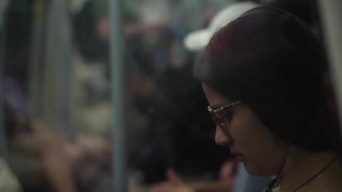Close shot of young attractive Ukraine female in glasses sitting on moving city metro train. Woman calling typing text message on mobile phone. Pretty Lady waving hands say goodbye. Traveling alone.