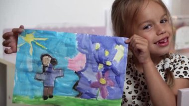 Talented Creative Child Girl Female Artist Draws Ranbow Mother summer on Paper, Child showing her work.Creates Colorful, Kid Drawing on table at Home. Painter Creating Abstract Modern Art. Childhood.