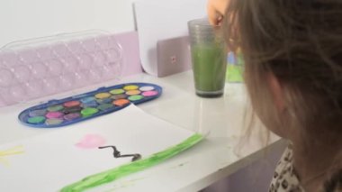 Talented Creative Child Girl Female Artist Draws with Her Hands on Paper, Using Fingers Paints Brush Creates Colorful, Kid Drawing on table at Home. Painter Creating Abstract Modern Art. Childhood.