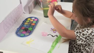 Talented Creative Child Girl Female Artist Draws with Her Hands on Paper, Using Fingers Paints Brush Creates Colorful, Kid Drawing on table at Home. Painter Creating Abstract Modern Art. Childhood.