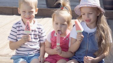 Three cute little Children enjoys delicious ice cream cone. Child eating watermelon popsicle. Kids Siblings snack sweets in Home Garden. Summer holiday Hot weather Sunny Day. Childhood, Food Candy.