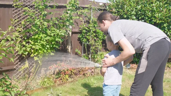 父と息子 庭の家の裏庭でパパと面白い男の子の散水芝生の植物 夏の家の仕事だ 勤勉な幼稚園屋外の子供 子供は家事を手伝う 子供のための活動 — ストック写真