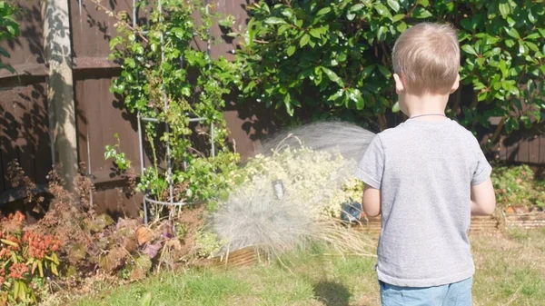 庭の住宅裏庭に面白い男の子の散水芝生の植物 暑い夏の屋外で灌漑ホースで遊ぶ愛らしい子供 子供は家事を手伝う 子供のための活動 幼少期 — ストック写真