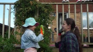 Çocuklu anne ev hanımı iş eldiveni takıyor çiçek dikmek için toprağı hazırlıyor beş kişi de işi bitirip sarılıyor. Çevre Aile Doğası kavramının ekilmesine yardım.