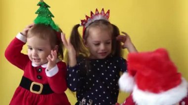 Sevimli, mutlu, neşeli 3 kardeş, kız kardeş ve Noel Baba kostümlü çocuk sarı arka planda kameraya bakınıyor. Çocuklar Noel 'i kutluyor. Çocuk Yılbaşını Eğlenerek Geçiriyor.