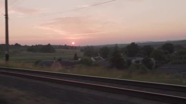 Pencereden yüksek hızlı tren manzarası güzel doğa manzarası vahşi arazi ve orman rayları yaz arkaplanında akşam günbatımında tren rayları. Ulaşım, seyahat, demiryolu, iletişim konsepti