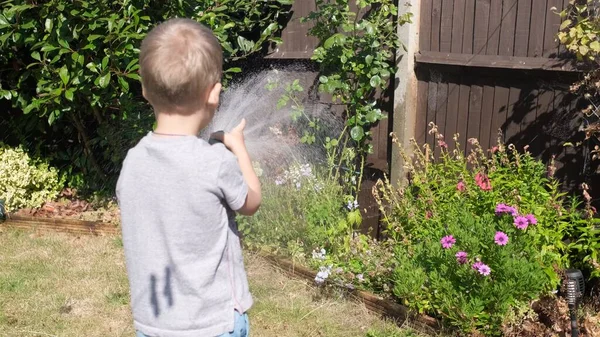 庭の住宅裏庭に面白い男の子の散水芝生の植物 暑い夏の屋外で灌漑ホースで遊ぶ愛らしい子供 子供は家事を手伝う 子供のための活動 幼少期 — ストック写真