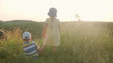 Sevimli anaokulu kızı ve oğlu gün batımından önce uzun otların arasında dağın tepesinde oturuyorlar. Vahşi çayırlarda yürüyen bir çocuk. Dağlarda mutlu bir çocuk. Çocukluk, doğa, yaşam tarzı, yaz konsepti