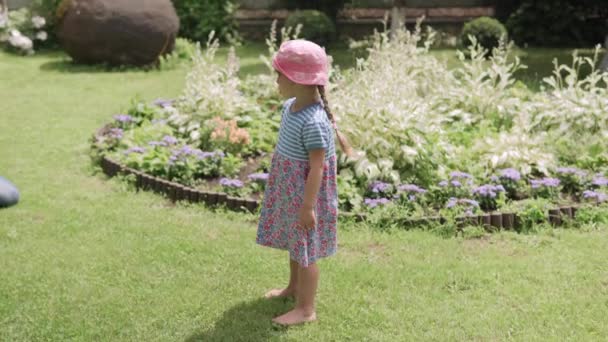 笑顔かわいいプリスクールガールが楽しそうに回転しています 花のドレスの娘は 晴れた夏の日にイディリック郊外の家の裏庭芝生でゲームを楽しむことができます 幼少期の家族の概念 — ストック動画