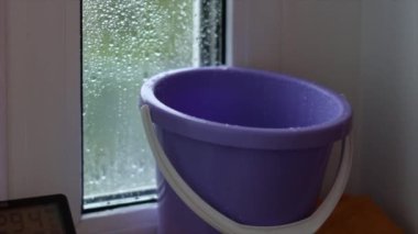 Çatı ya da balkon şiddetli yağmur nedeniyle sızdırıyor, damlalar kovaya damlıyor. Yakın plan. Acil durum konut, arıza, tamirat kavramı. Daha sonra dengelenmiş elle ateş etme..