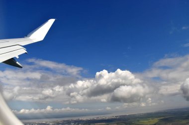 See-through aircraft window to beautiful blue sky with white clouds floating above land on a sunny day.