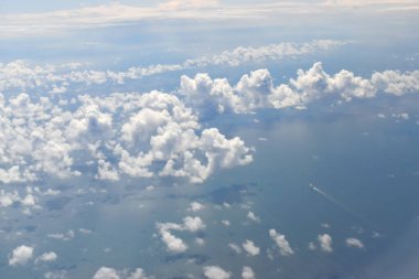 Viewed from the airplane window at a high altitude,  with the beautiful landscape with white clouds floating over the sea with clear water and a small boat running on surface water.