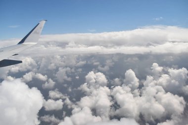Airplane wing flying above a dramatic sky with the landscape of white clouds viewed from a high altitude. Viewed from the airplane window.
