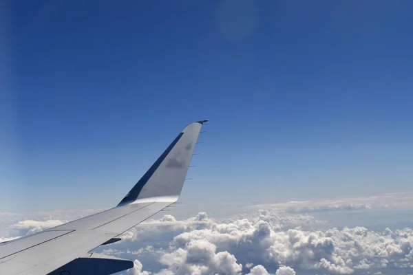 An aircraft wing above cloud scrap with the beautiful blue color of the horizon in the blue sky, view from an airplane window.