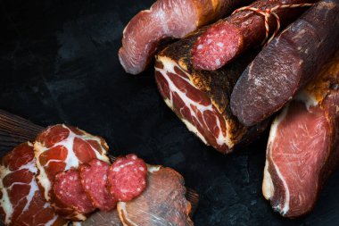 Jambon, sosis, jambon, jambon, siyah arka planda pastırma. Etli meze, pankart, menü. Boşluğu kopyala.