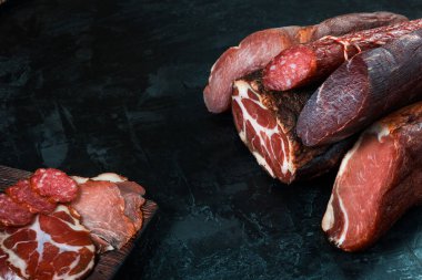 Jambon, sosis, jambon, jambon, siyah arka planda pastırma. Etli meze, pankart, menü. Boşluğu kopyala.