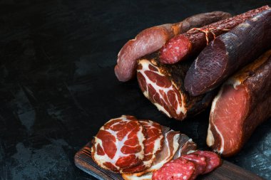 Jambon, sosis, jambon, jambon, siyah arka planda pastırma. Etli meze, pankart, menü. Boşluğu kopyala.