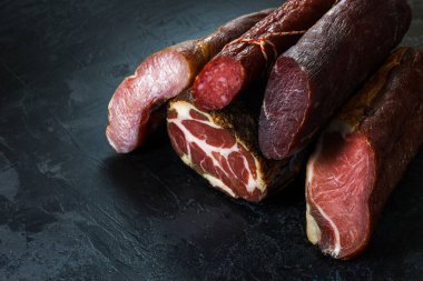 Jambon, sosis, jambon, jambon, siyah arka planda pastırma. Etli meze, pankart, menü. Boşluğu kopyala.