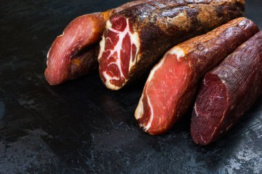 Jambon, sosis, jambon, jambon, siyah arka planda pastırma. Etli meze, pankart, menü. Boşluğu kopyala.