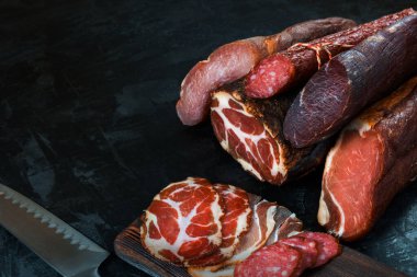 Jambon, sosis, jambon, jambon, siyah arka planda pastırma. Etli meze, pankart, menü. Boşluğu kopyala.