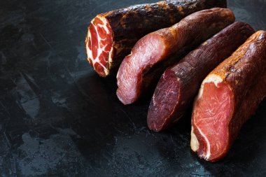 Jambon, sosis, jambon, jambon, siyah arka planda pastırma. Etli meze, pankart, menü. Boşluğu kopyala.