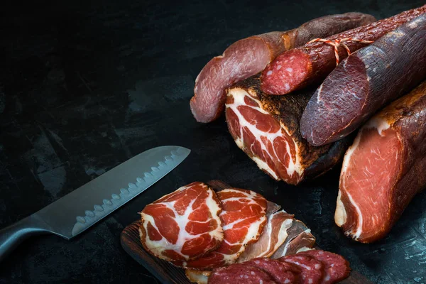 Jambon, sosis, jambon, jambon, siyah arka planda pastırma. Etli meze, pankart, menü. Boşluğu kopyala.